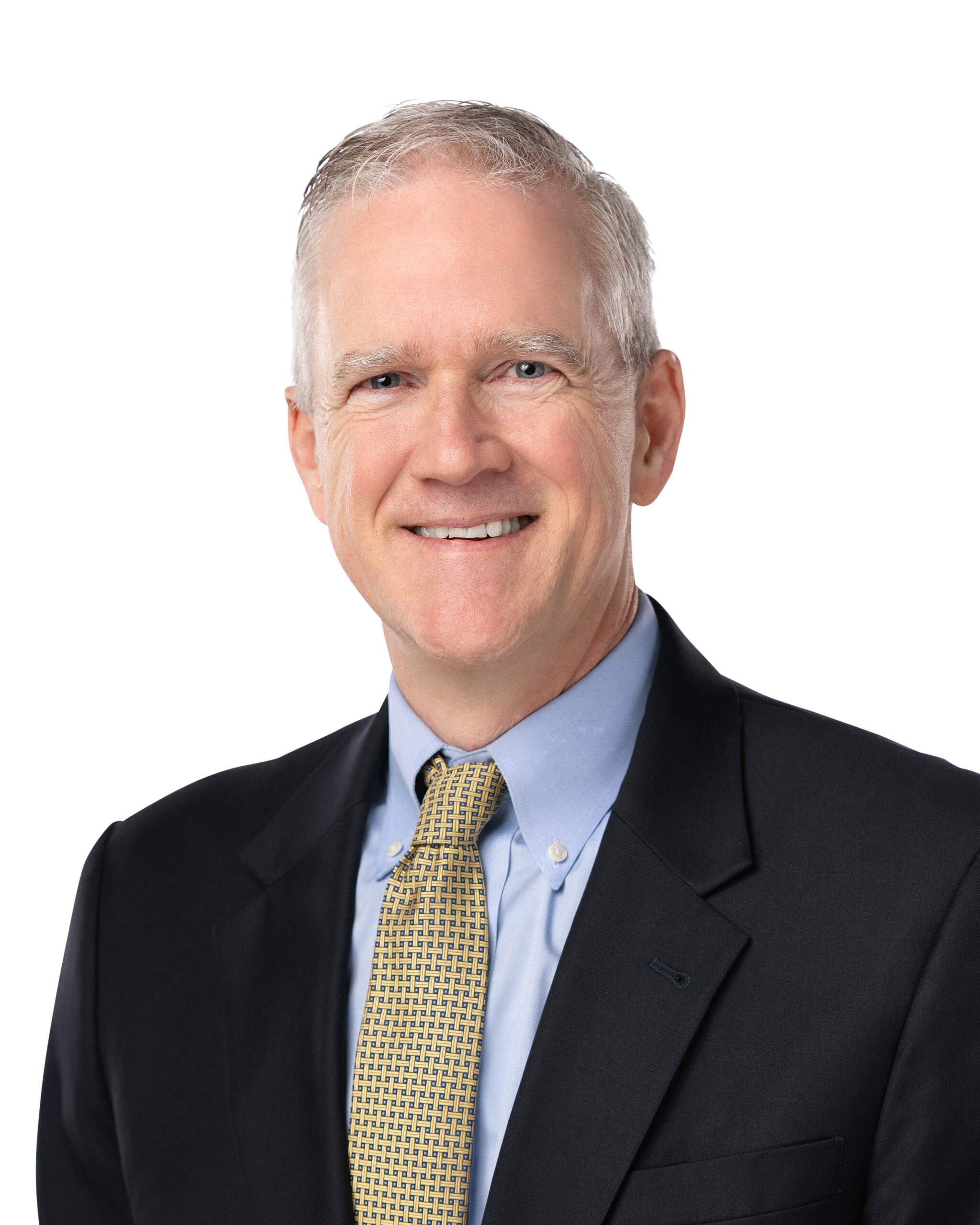 Professional lifestyle headshot of Mike Lipscomb. He has a warm smile, wearing a black blazer over a light blue button-down shirt. and gold tie.