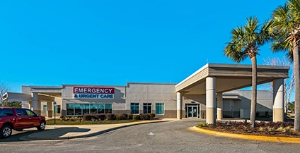 Emergency and urgent care facility with a covered entrance and palm trees. A red SUV is parked nearby under a clear blue sky.