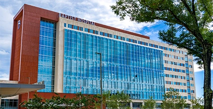 A modern hospital building with reflective blue glass windows and brick accents, set against a partly cloudy sky, conveying a sense of care and professionalism.