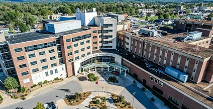 Aerial view of a large hospital complex with multiple connected brick buildings. A semi-circular entrance is prominent, surrounded by landscaped gardens.