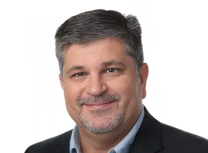 Headshot of James Patrick Capes, smiling, wearing a black blazer and a blue button-down shirt.