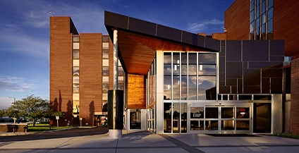 Modern building with a mix of glass and brick facade under a blue sky. The entrance features large windows and angled roof, creating a welcoming feel.