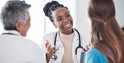 A smiling doctor with a stethoscope converses warmly with a patient in a blue shirt, creating a friendly and reassuring atmosphere in a clinic setting.