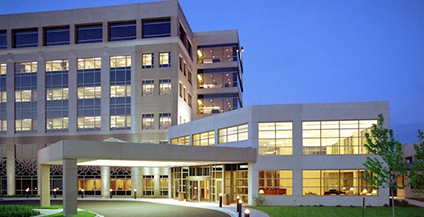 A modern hospital building at dusk with illuminated windows, featuring a multi-story structure and main entrance, conveying a welcoming atmosphere.