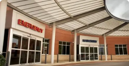 Entrance to a hospital emergency department with large glass doors. The words 