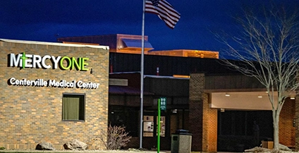 Exterior of MercyOne Centerville Medical Center at night with illuminated signage. An American flag waves above, adding to the calm evening setting.