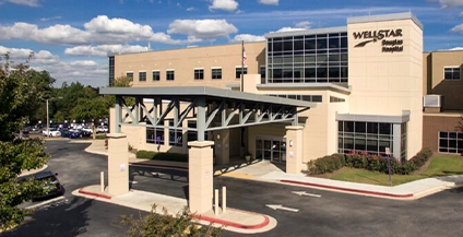 Exterior view of Wellstar Douglas Hospital showing the main entrance under a grey metal canopy and the prominent building signage against a blue sky.