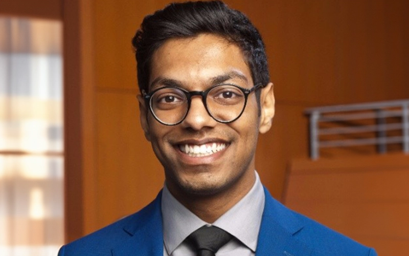 Professional headshot of Aadil Vora, a man with glasses wearing a dark suit jacket over a light blue button-down shirt.