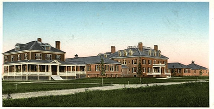 Vintage image of a Anna Jaques two-story brick building complex with multiple chimneys and wraparound porches, set against a clear sky and surrounded by grassy fields.