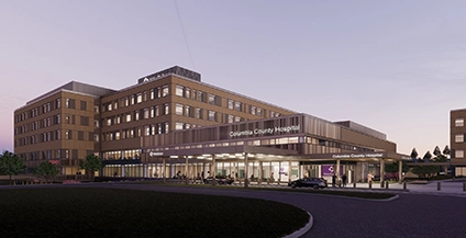 Exterior view of Columbia County Hospital at dusk. The modern building has multiple floors, large windows, and a warmly lit entrance, creating an inviting atmosphere.